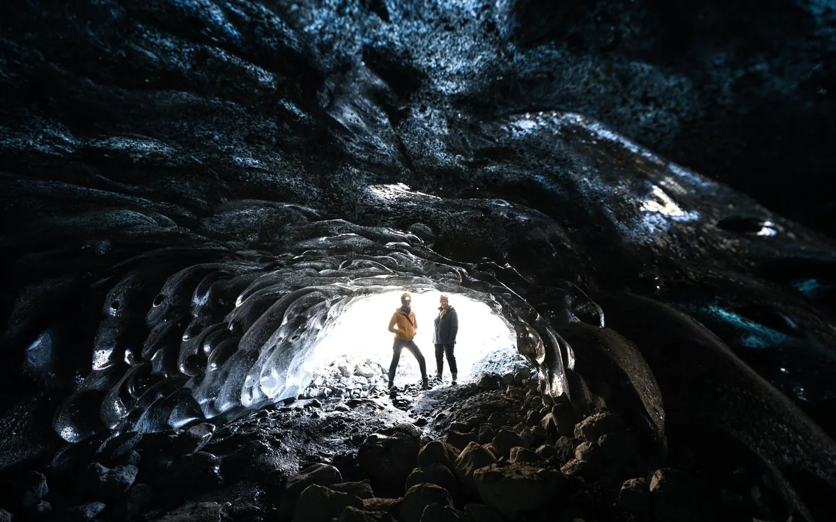 Personas de pie en la entrada de una cueva de hielo bajo un glaciar en Islandia