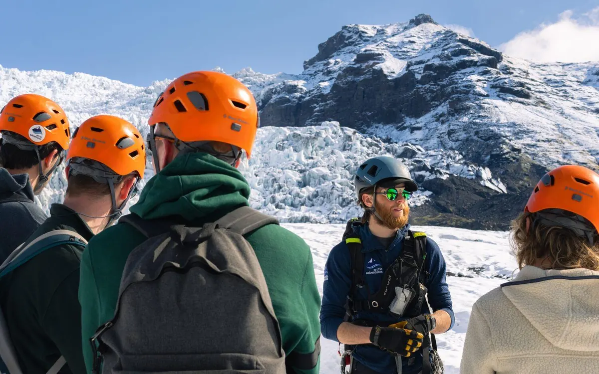 Personen mit orangefarbenen Helmen beim Anlegen von Steigeisen vor einer Gletscherwanderung in Skaftafell