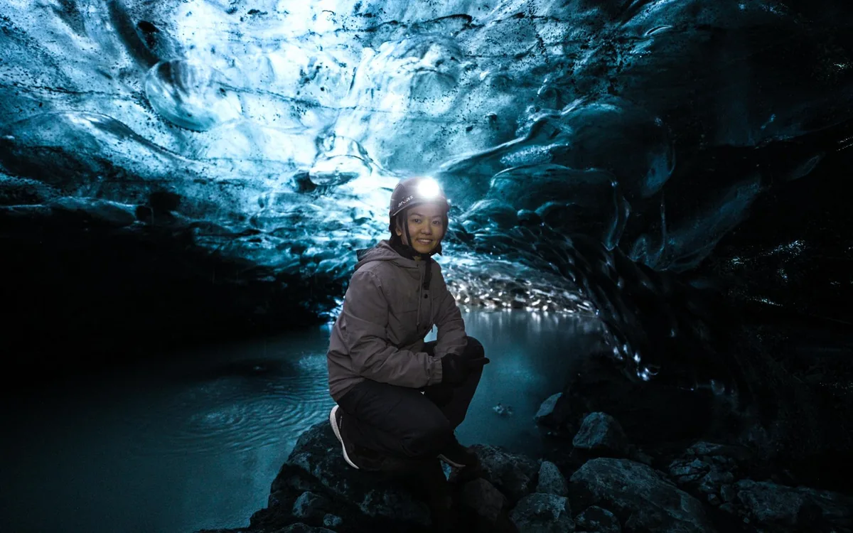 A blue ice arch inside a glacier in Iceland with a person standing beneath it
