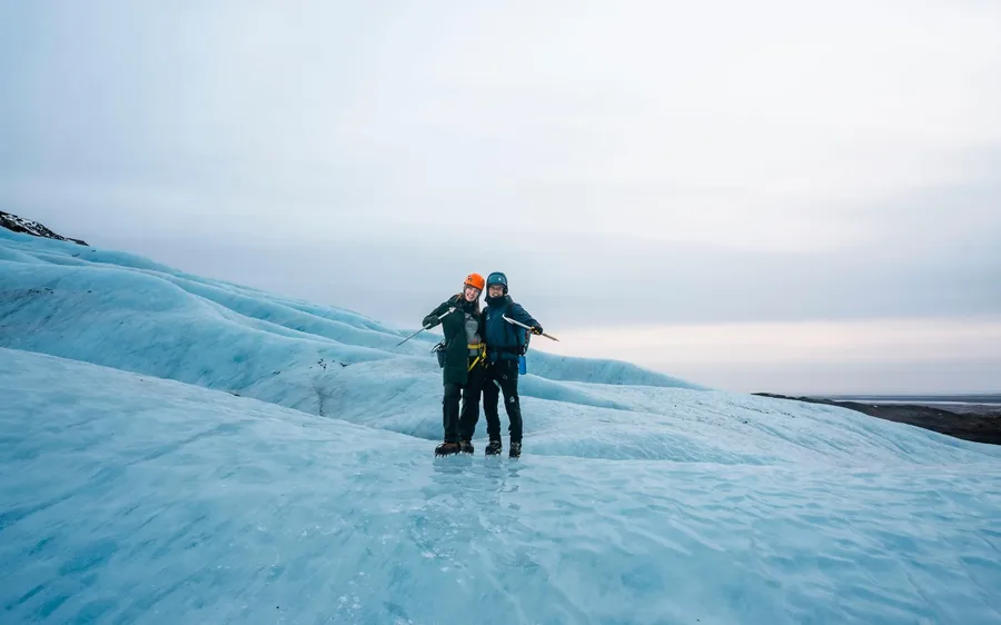 Dos personas con cascos naranjas caminando sobre el hielo azul del glaciar Vatnajokull, Islandia
