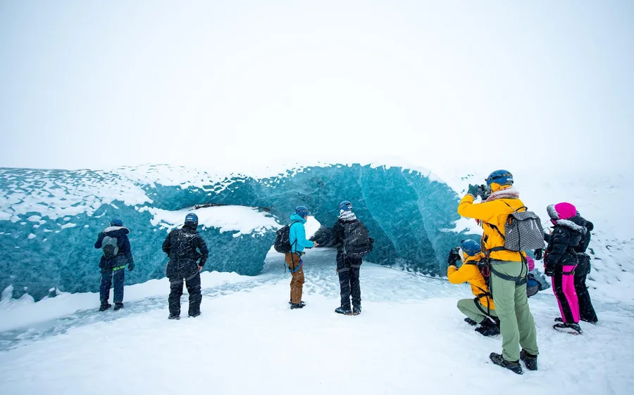 Personas de pie junto a una pared de hielo azul dentro de un glaciar en Islandia