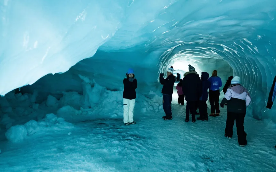 Visitantes caminando por un túnel de hielo azul iluminado dentro del glaciar Langjokull