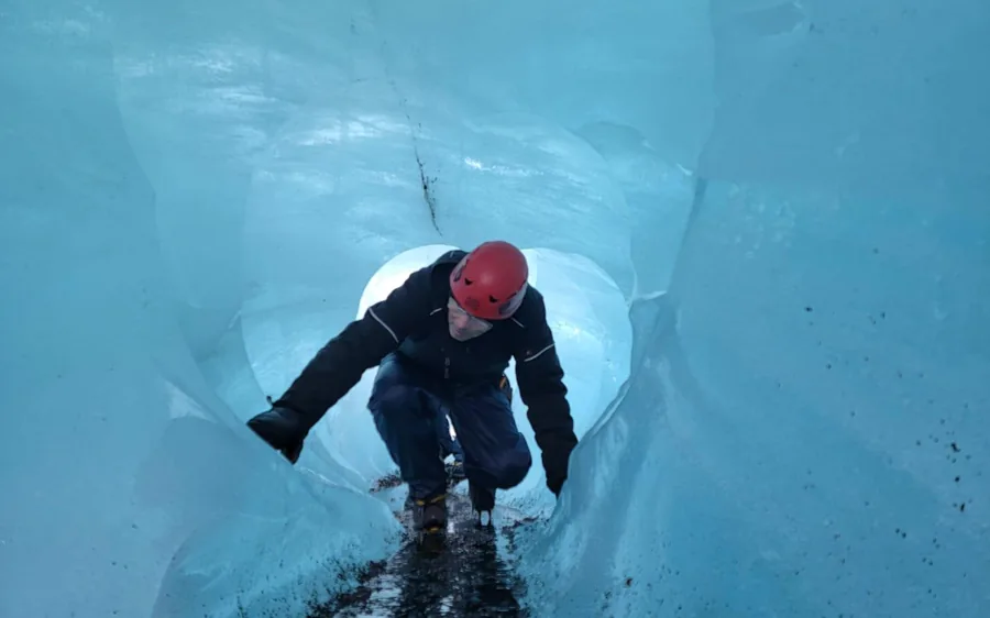 Un visitante de pie en una cueva de hielo azul a la que se llega en súper jeep en Islandia