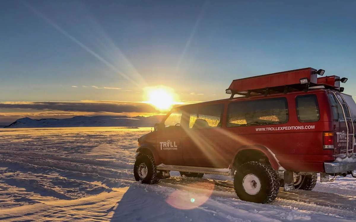 Un super jeep aparcado sobre arena negra frente a un glaciar en Islandia al atardecer