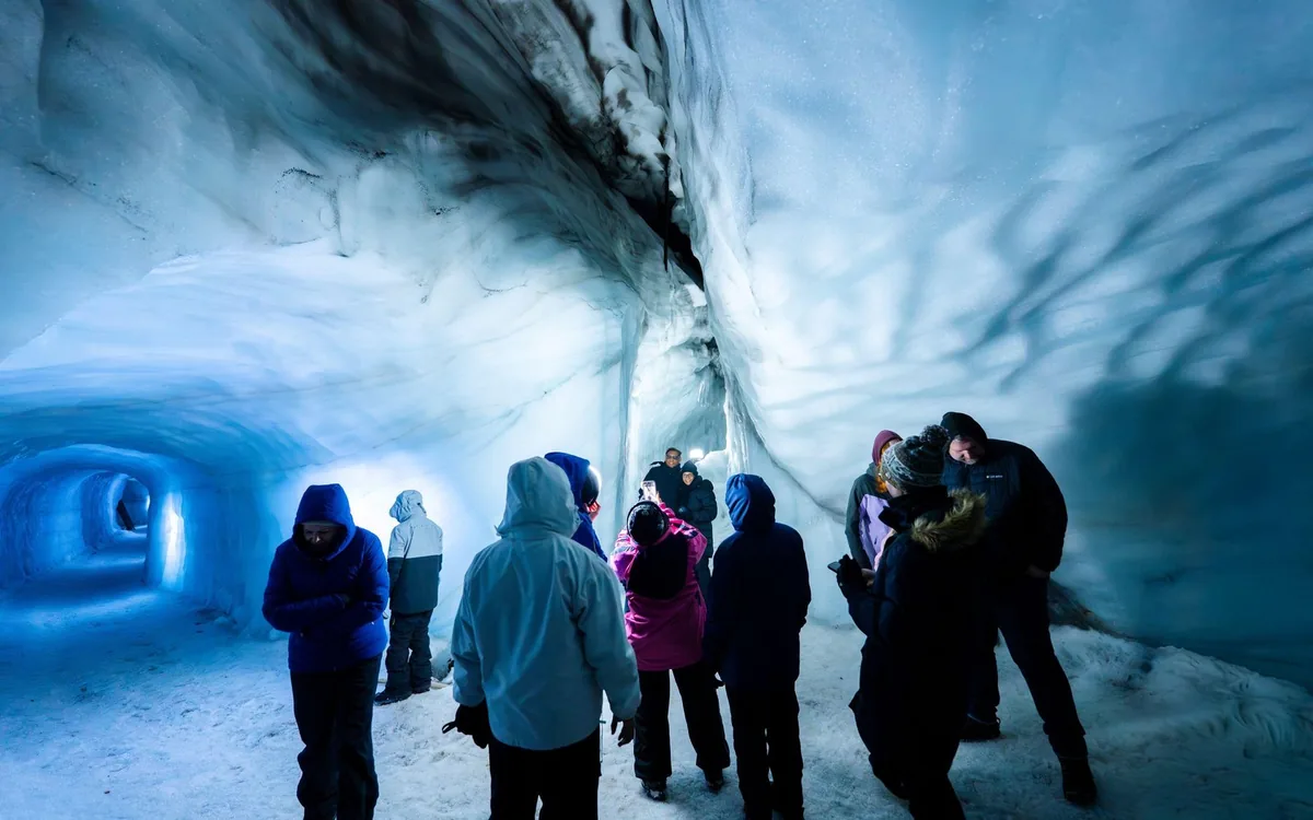 Besucher gehen durch einen beleuchteten blauen Eistunnel im Langjokull in Island
